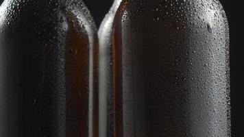 Three very cold beer bottles rotating on black background. Close up video