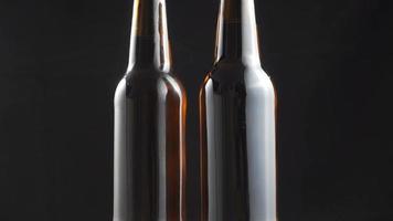Two beer bottles rotating on black background. video