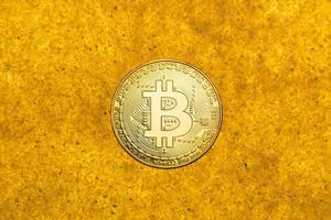 one bitcoin crypto coin on a shiny golden sand background with backlight, top view photo