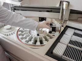 the girl in the lab puts the serum samples in a medical device for analysis. Machine automatic biochemical analysis. Indoors. photo