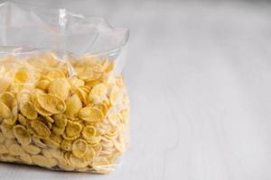 Cornflakes in plastic bag on white wooden surface photo