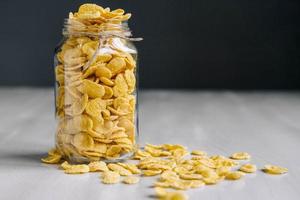 Cornflakes in a glass jar on white wooden surface