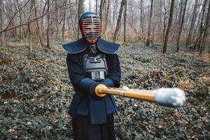 Hombre practicando kendo con espada de bambú shinai sobre fondo de bosque foto