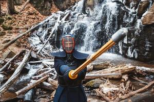 Hombre practicando kendo con espada de bambú en cascada, rocas y fondo de bosque foto