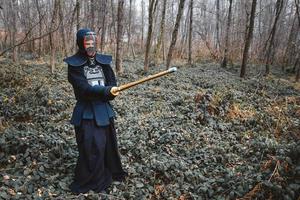 Hombre practicando kendo con espada de bambú shinai sobre fondo de bosque foto