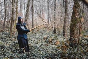 Man practicing kendo with shinai bamboo sword on forest