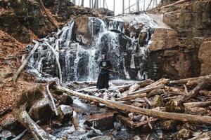 Hombre practicando kendo con espada de bambú en cascada, rocas y fondo de bosque foto