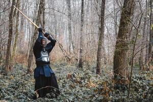 Hombre practicando kendo con espada de bambú shinai sobre fondo de bosque foto