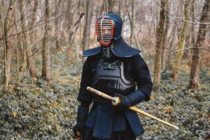 Hombre practicando kendo con espada de bambú shinai sobre fondo de bosque foto