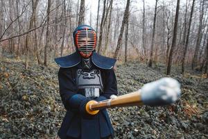 Hombre practicando kendo con espada de bambú shinai sobre fondo de bosque foto