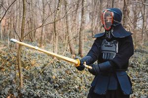 Man practicing kendo with shinai bamboo sword on forest background photo