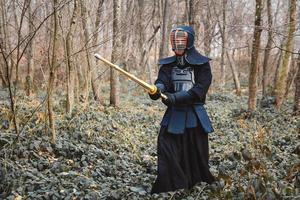 Hombre practicando kendo con espada de bambú shinai sobre fondo de bosque foto