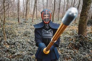 Hombre practicando kendo con espada de bambú shinai sobre fondo de bosque foto