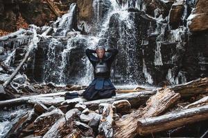 Hombre practicando kendo con espada de bambú sobre fondo de cascada foto