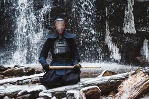 Man practicing kendo with bamboo sword on waterfall background photo