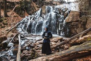 Hombre practicando kendo con espada de bambú en cascada, rocas y fondo de bosque foto