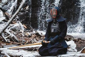 Hombre practicando kendo con espada de bambú sobre fondo de cascada foto