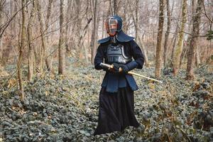 Hombre practicando kendo con espada de bambú shinai sobre fondo de bosque foto