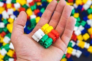 Hand with colorful plastic bricks and details of toys on a colorful background photo