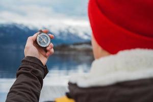 Traveler man holds an old compass against background of the mountain and a lake