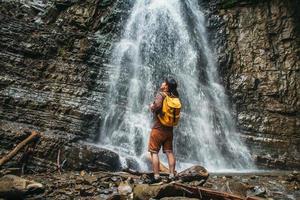 Man with a yellow backpack standing on background of a waterfall photo