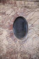 Ventana circular en el lateral de un edificio de ladrillo rodeado de hiedra
