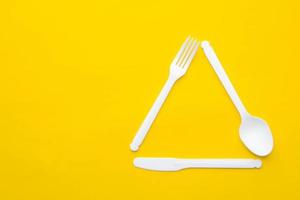 Plastic white fork, knife and spoon in the form of a triangle on yellow background photo