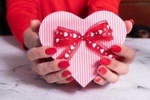 caja de regalo rosa en forma de corazón para el día de san valentín con mano de mujer manicura roja mate foto
