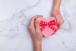 Caja de regalo rosa en forma de corazón para el día de San Valentín con vista superior de manos masculinas y femeninas foto