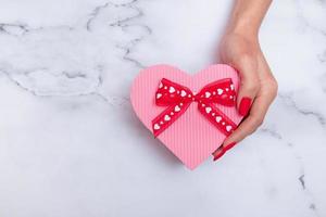 Caja de regalo rosa en forma de corazón para el día de San Valentín con mano de mujer vista superior de manicura mate roja foto