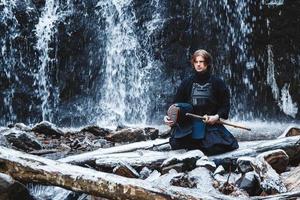 Hombre practicando kendo con espada de bambú sobre fondo de cascada foto