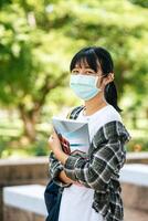 Female students wear masks, stand on stairs and hold books. photo