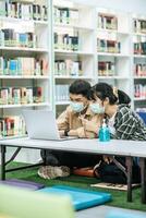 Men and women wear masks and use a laptop to search for books in the library. photo