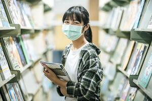 una mujer con una máscara y buscando libros en la biblioteca. foto