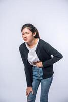 A woman standing with a stomach ache and presses her hand on her stomach. photo