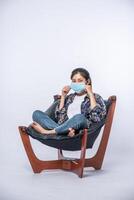 Una mujer incómoda sentada en una silla y con una máscara. foto