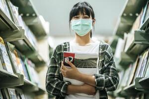 A woman wearing a mask and searching for books in the library. photo