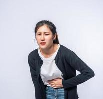 A woman standing with a stomach ache and presses her hand on her stomach. photo