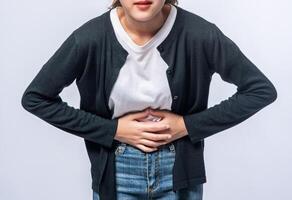 A woman standing with a stomach ache and presses her hand on her stomach. photo