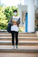 Female students wear masks, stand on stairs and hold books. photo