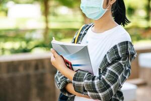 Female students wear masks, stand on stairs and hold books. photo