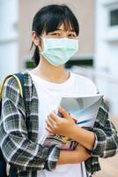 Female students wear masks, stand on stairs and hold books. photo