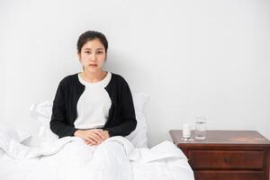 An uncomfortable woman sits on the bed and has medicine on the table. photo