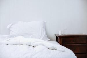 cama blanca con una mesa con cajones con frascos de medicinas y vaso de agua foto
