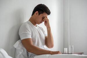 A man with migraines holds her hand by his nose in the bed. photo