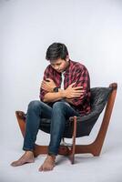 el hombre con una camisa a rayas se sienta enfermo y se sienta en una silla y se cruza de brazos. foto