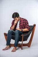el hombre con una camisa a rayas se sienta enfermo y se sienta en una silla y se cruza de brazos. foto