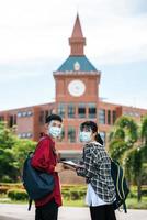 Male and female students wear masks and stand in front of the university.