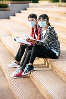 Male and female students wearing masks sit and read books on the stairs photo