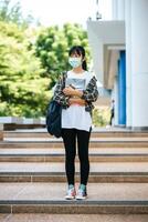 Female students wear masks, stand on stairs and hold books. photo